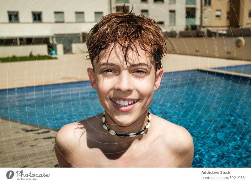 Happy Boy Smiling by the Poolside on a Sunny Day boy child smile pool swimming water sunny outdoors summer happiness wet hair shell necklace residential