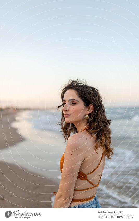 Young woman standing near sea beach wave evening dreamy coast seaside summer weekend female rest young water shore ocean relax long hair wavy hair feminine slim