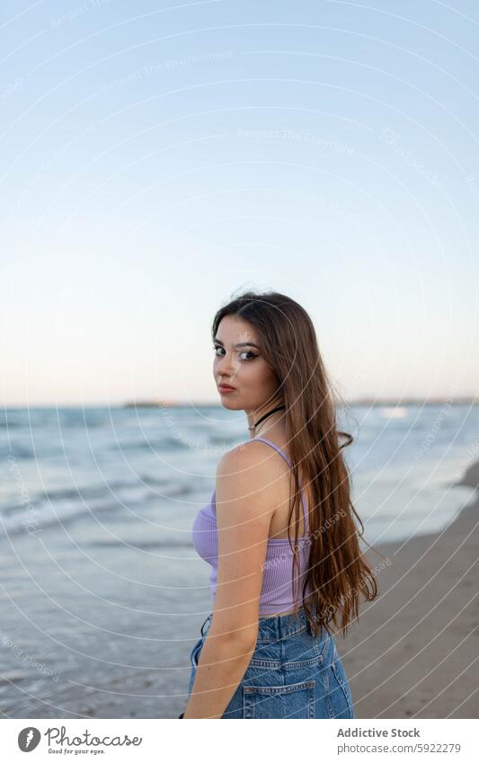 Young woman standing near sea beach wave evening dreamy coast seaside summer weekend female rest young water shore ocean relax long hair wavy hair feminine slim