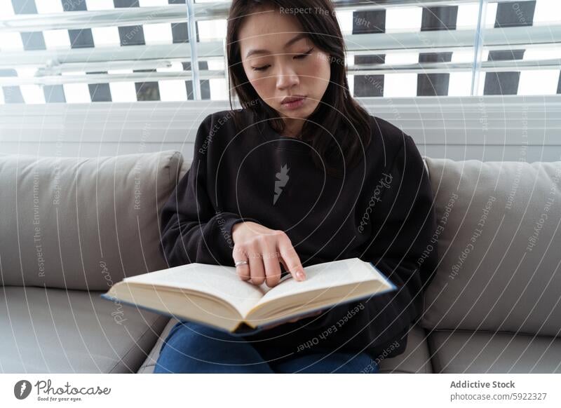 Serene moment of a woman engrossed in a book reading couch sit serene absorbed literacy relax indoor home casual leisure lifestyle study concentration focus