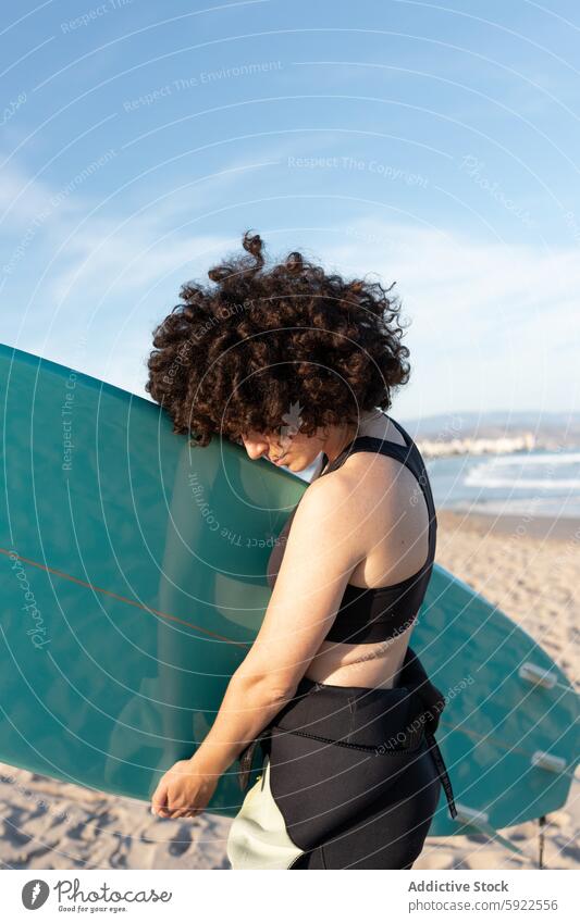 Curly haired woman with surfboard on sea shore surfer tropical beach wave foam carefree activity female seashore wetsuit coast water cloudless sky bay scenery