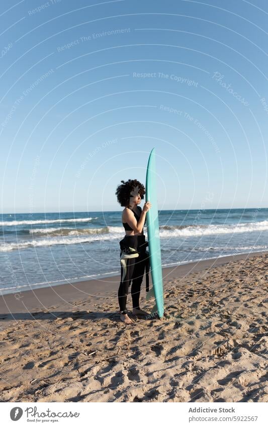 Curly haired woman with surfboard on sea shore surfer tropical beach wave foam carefree activity female seashore wetsuit coast water cloudless sky bay scenery