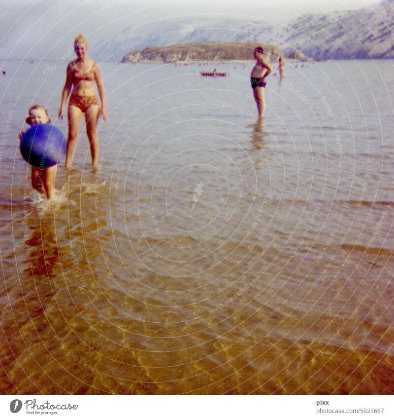 Vacation by the sea in the early 70s | Woman in a bikini runs through the shallow water behind a little girl with a beach ball in her hands Adriatic Sea