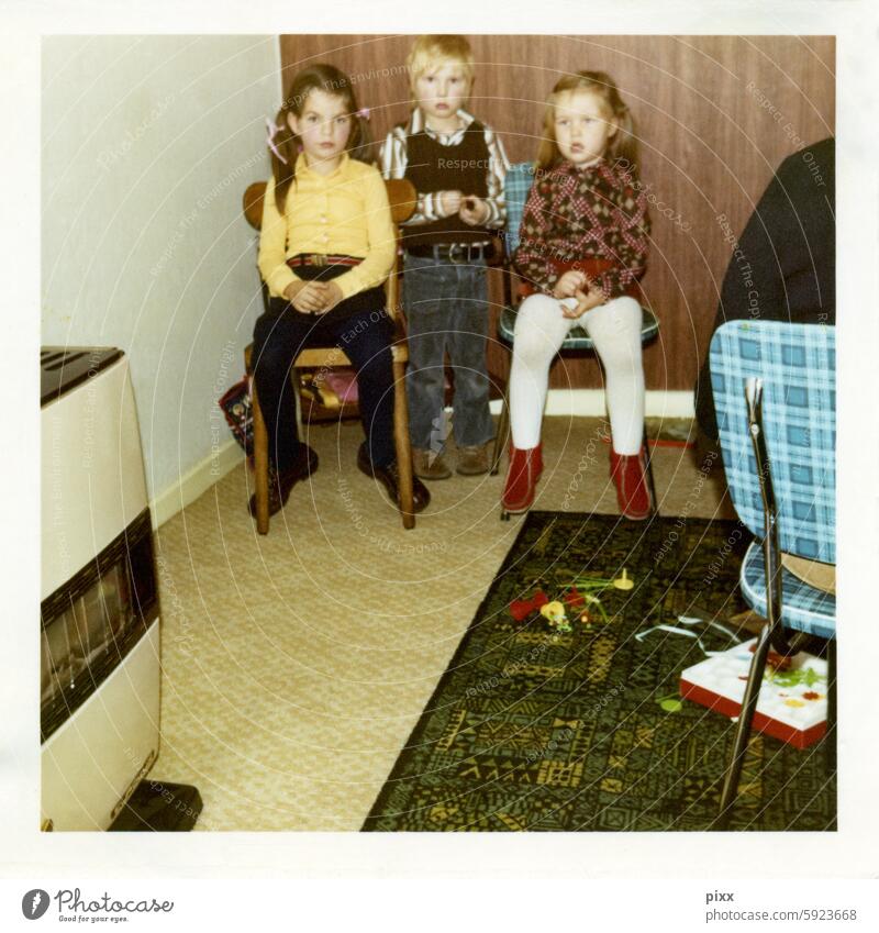 Polaroid from the 70s showing three children in front of a wooden wallpaper Playing Boredom unwilling bored PVC kitchen chair midcentury Flower power checks