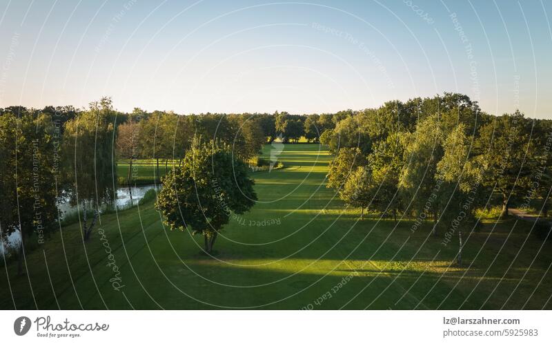 A tranquil aerial view of a lush golf course fairway, bathed in the warm glow of sunset. Ideal for themes of relaxation, nature, and sports, this image captures the peaceful beauty of the golfing experience.