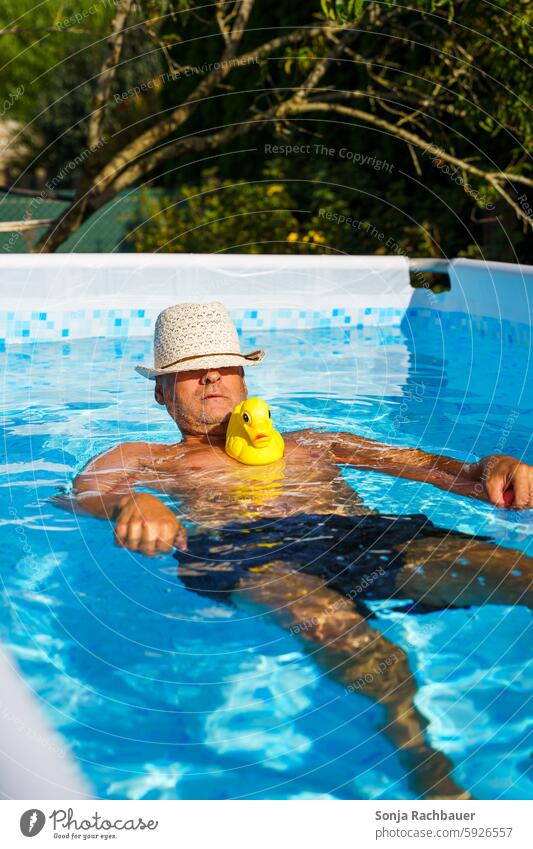 A man with a sun hat and a yellow rubber duck in a pool. Man Summer Relaxation Swimming & Bathing Vacation & Travel Summer vacation Water Refreshment