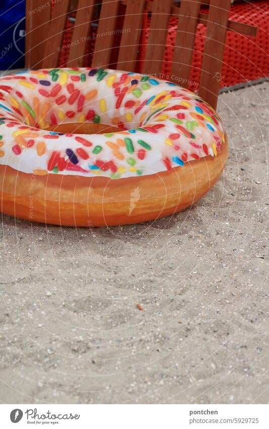 a donut on the beach in front of a beach chair. swimmers Floating tyres doughnut Humor Red Sand Beach chair North Sea vacation Vacation & Travel Tourism