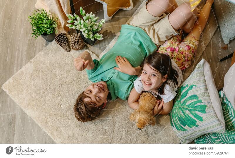 Children laughing and relaxing lying over rug in cozy tent at home surrounded by cushions and plants happy children carpet resting boy pointing finger up little