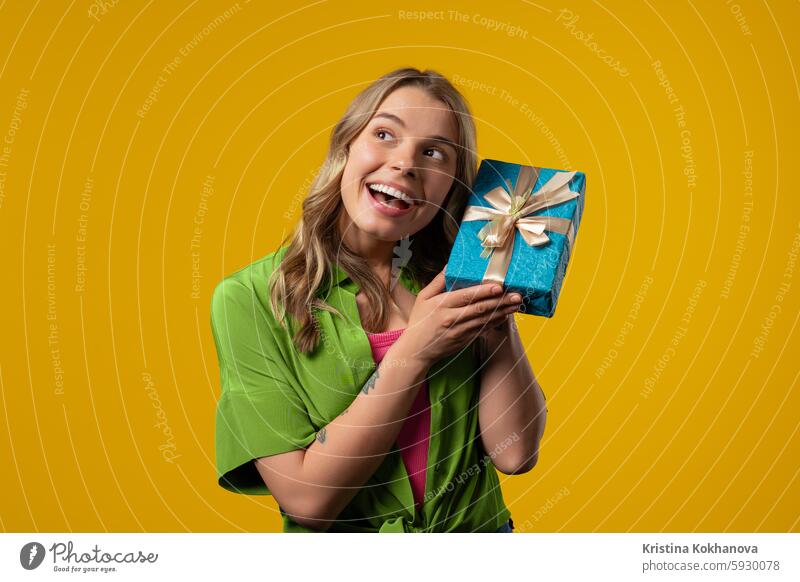 Happy woman gift box on yellow background. Lady smiling,interested what's inside adult attractive beautiful beauty birthday celebrating celebration cheerful