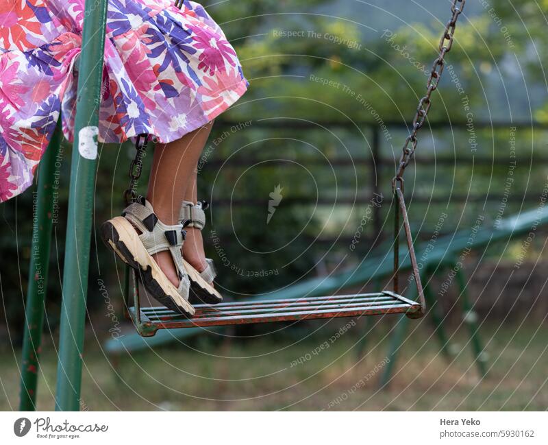 little girl dressed in summer playing on an old swing in nature alone childhood colors flowers fun green loneliness outdoors park sandals lifestyle happiness