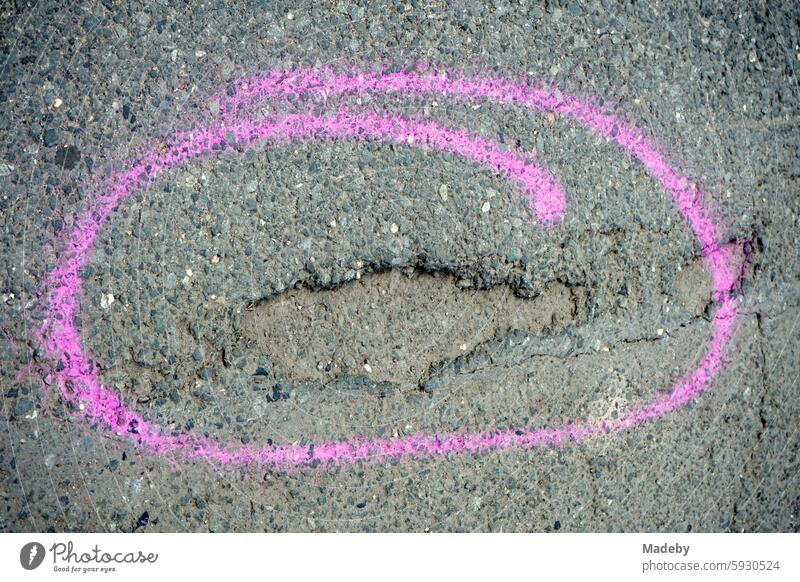 Deep pothole in gray asphalt marked with a sweeping hand-painted circle in purple in summer sunshine in Hafenweg in Münster in Westphalia in Münsterland