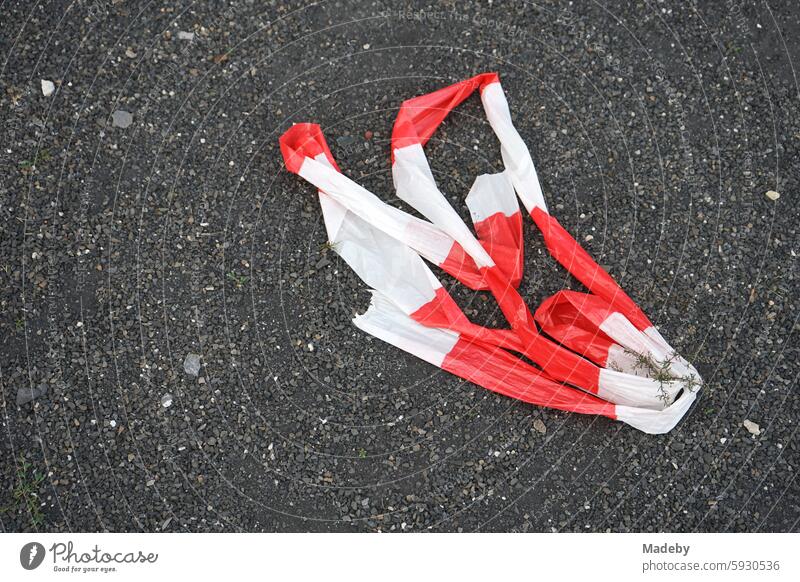 Torn barrier tape in red and white on gray asphalt in summer at the Golden Oldies classic car meeting in Wettenberg Krofdorf-Gleiberg near Gießen in Hesse