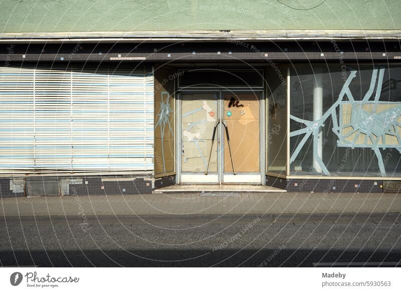 Vacant store with old blinds, emergency glazing and cracked shop window with adhesive tape in the sunshine on Krofdorfer Straße in Giessen in Hesse Cast