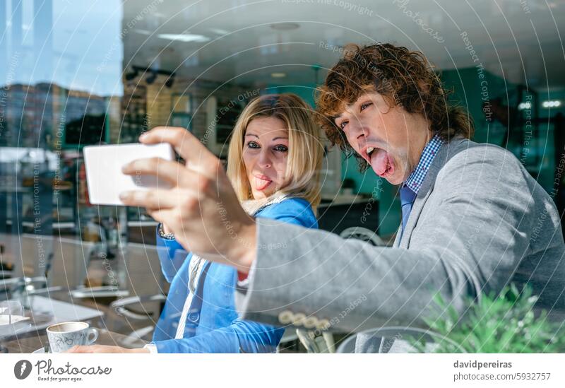 Coworkers taking a selfie coworkers business funny grimace tongue playing fool photo smiling smartphone break coffee cafe pause young people cup friends man