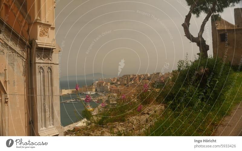 On the left, part of Gaeta Cathedral (Italy) On the right, an old building and the silhouette of an umbrella line. In between the view of the old town and the port of Gaeta.