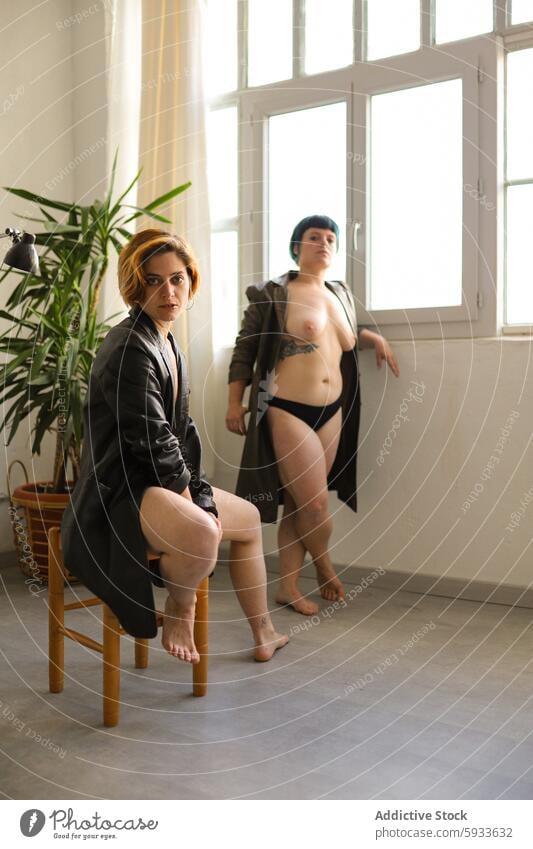 Two sisters in contrasted attire in bright room confidence style light window plant expression serious contemplative mood outfit fashion pose identity seated