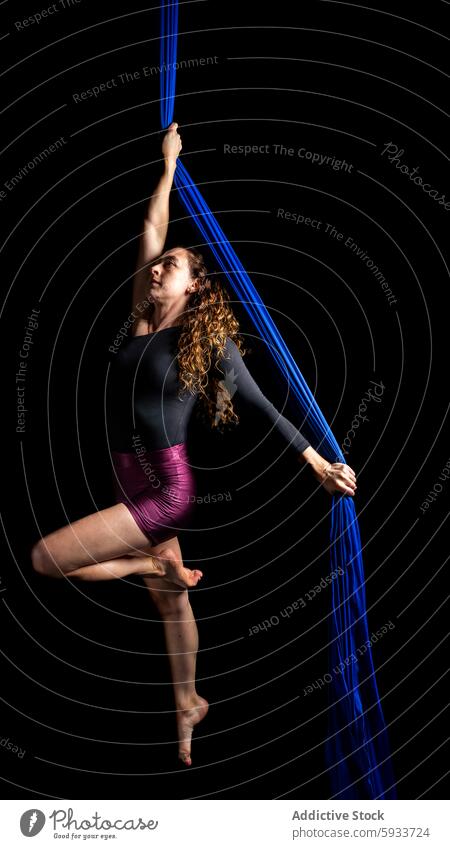 Aerial dancer performs elegant modern dance on blue silk aerial woman flexibility strength performance suspended fabric acrobat gymnastics art movement grace