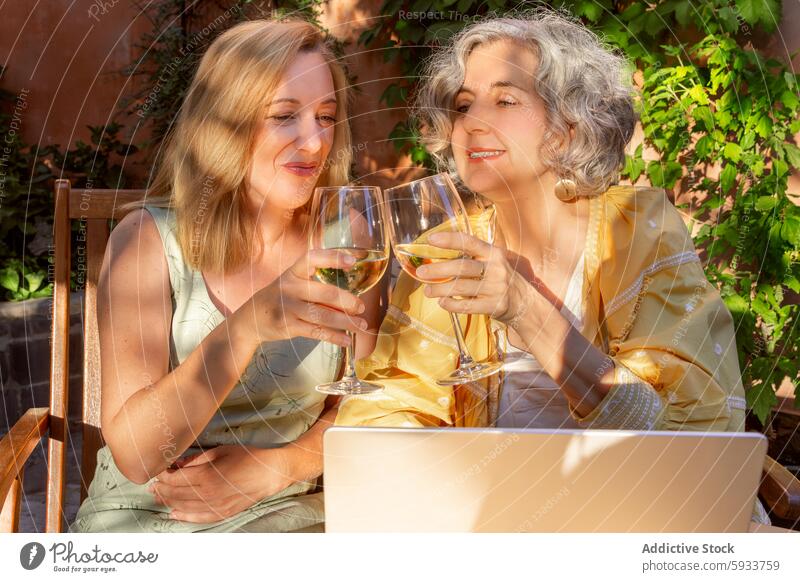 Elderly and middle-aged women enjoying wine outdoors elderly white wine conversation garden sunny laptop leisure talking beverage drinking friendship together