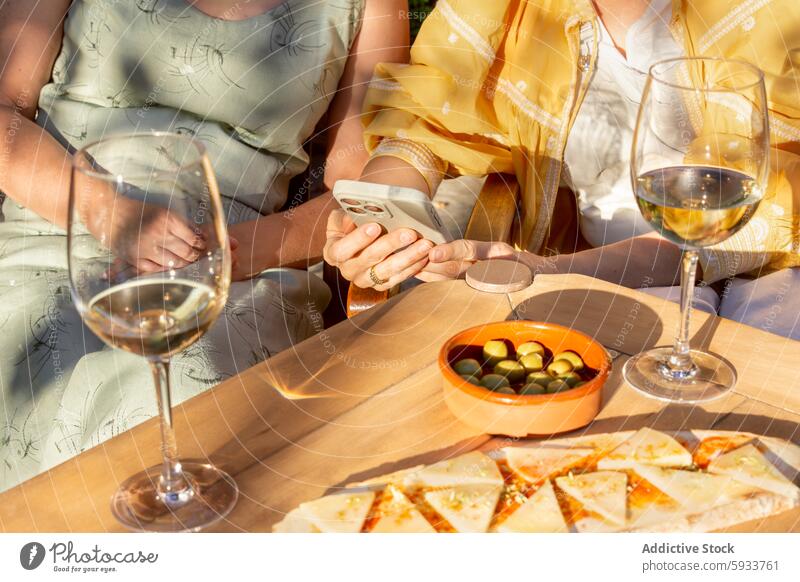 Two women enjoying a leisurely afternoon with wine outdoors mature senior friendship drinking garden table glass summer smartphone smiling enjoyment bonding