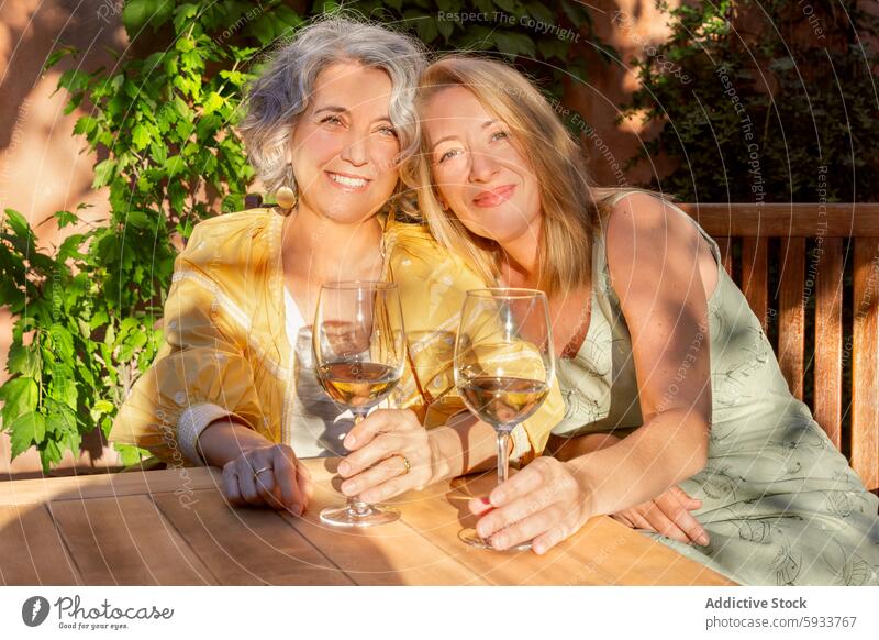 Senior women enjoying wine outdoors in sunlight senior toast glass smile table wooden friendship leisure drink alcohol celebration senior citizen female sit