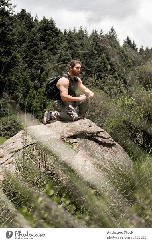 Man contemplating nature while seated on a rocky outcrop man forest outdoors hiker contemplation greenery serious muscular backpack sitting adventure athletic