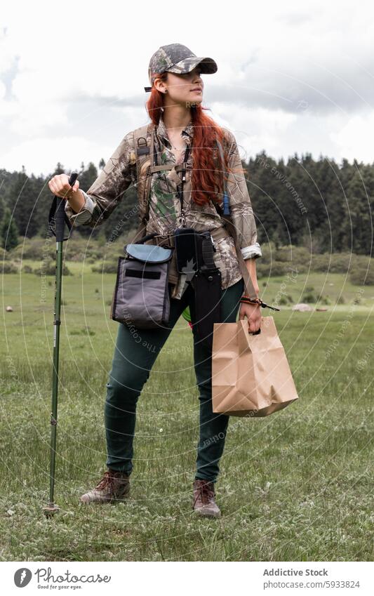 Hiker with gadgets and paper bag in the woods woman hiker forest outdoor nature trekking walking stick caucasian looking away device adventure exploration