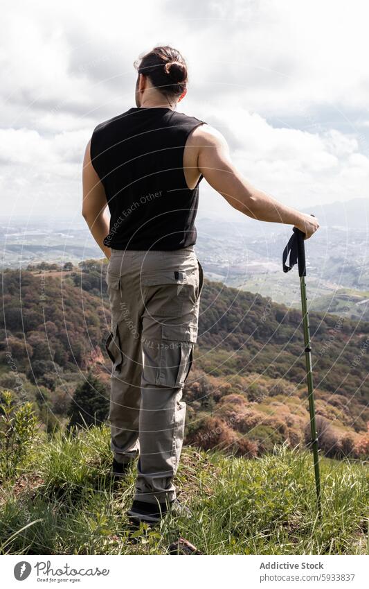 Back view of man standing in nature with hiking stick back view unrecognizable anonymous faceless outdoor adventure landscape travel hill grass leisure