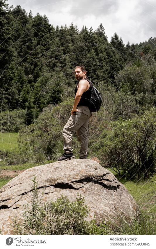 Young man hiking on a rocky terrain surrounded by lush greenery nature forest outdoors adventure leisure landscape casual attire backpack daytime confident