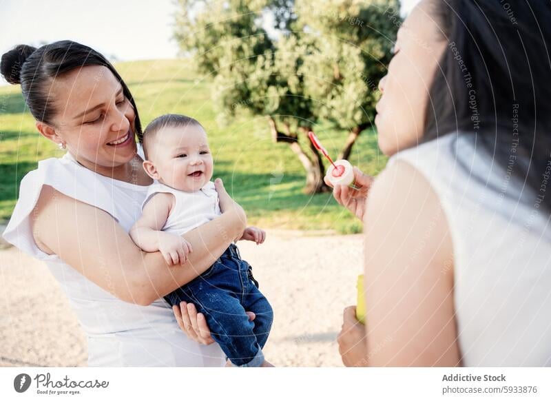 Lesbian couple enjoying a sunny day with their son lesbian woman family park infant happiness smile mother bubble outdoor parenting leisure activity tree grass