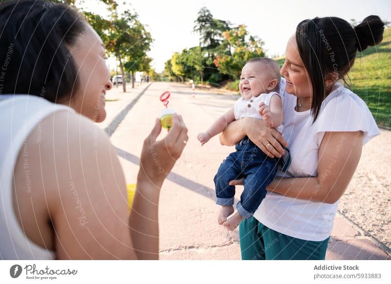 Generated image family lesbian couple woman mother son baby child park outdoor daytime summer casual clothing jeans t-shirt grass toy smiling happiness love