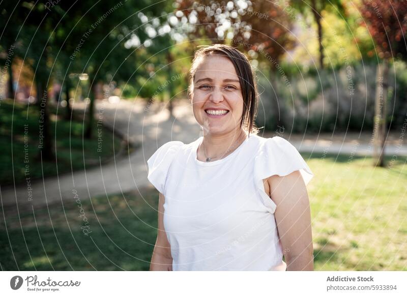 Casual colombian woman smiling in sunlit park with blurred tree background smile casual white blouse happy outdoor nature greenery portrait joyful sunlight path