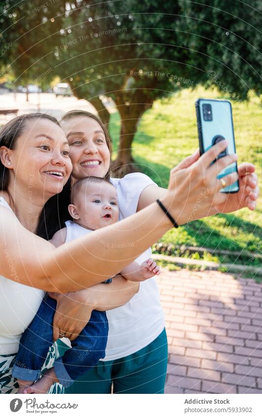 Lesbian couple with their son enjoying a selfie outdoors lesbian park family happiness smartphone tree woman mother child bonding technology social media happy