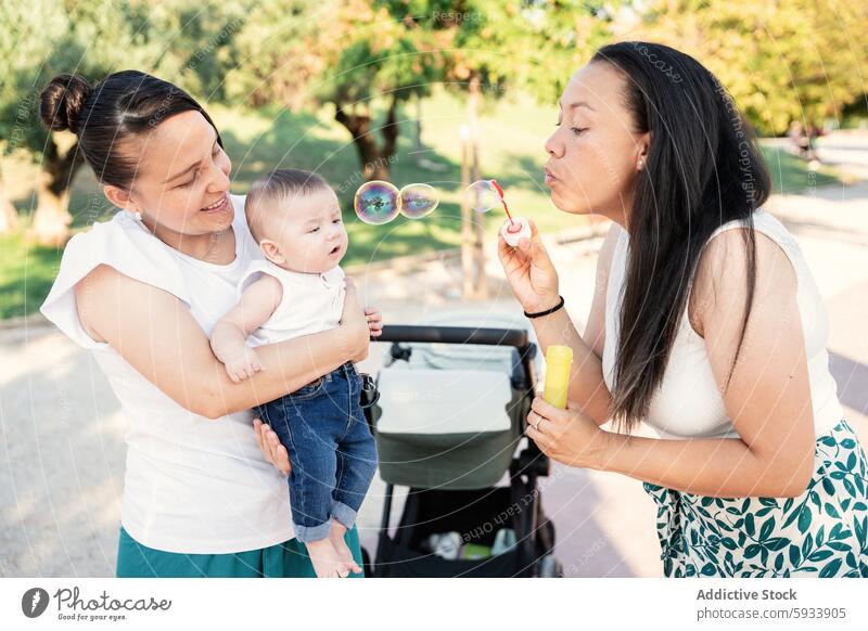 Lesbian couple enjoys a day with their son blowing bubbles lesbian woman baby mother park quality time holding watching smiling secure family outdoor casual