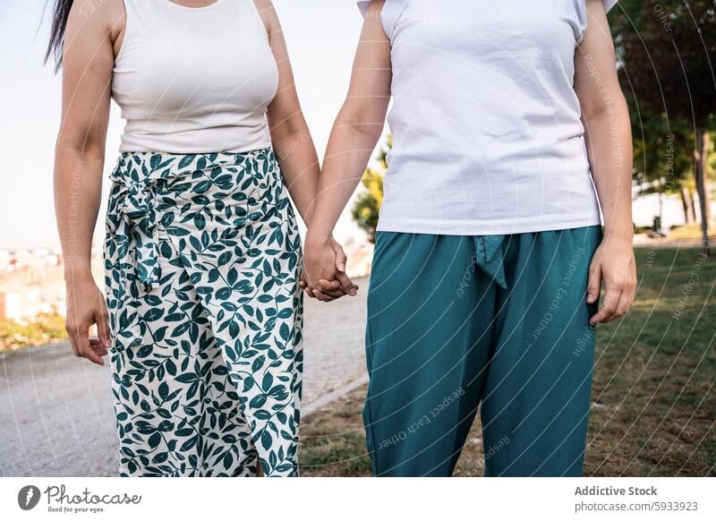 Lesbian couple holding hands outdoors in casual white tops and green pants lesbian lgbt colombian walking park serene sunny connection love relationship unity