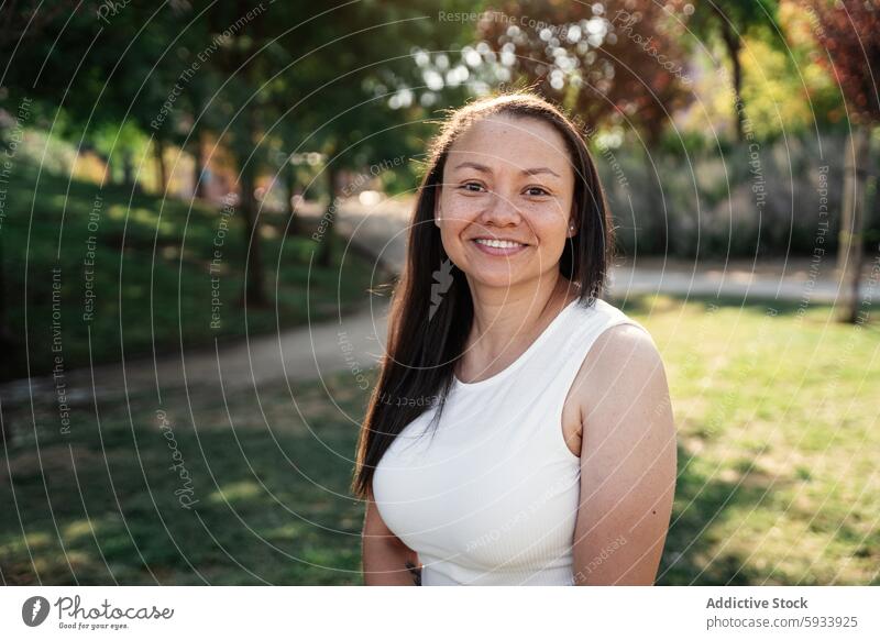 Portrait of smiling colombian woman enjoying a sunny day in a lush green park portrait smile tree outdoor nature happy summer bright casual white top sunlight