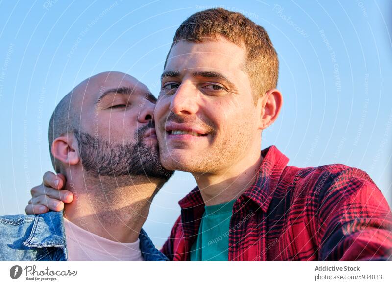 Affectionate moment between a gay couple outdoors love relationship man affection tenderness kiss happiness joy emotion support comfort male cheek clear sky