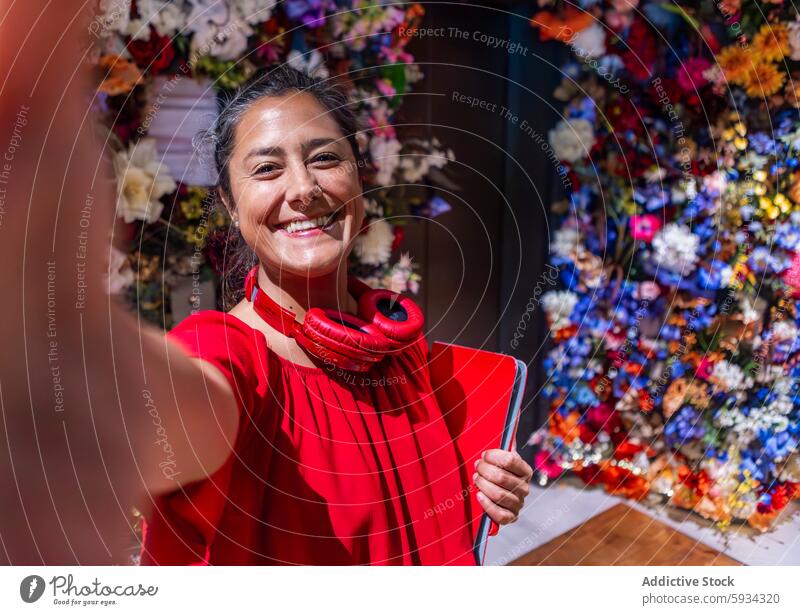 Happy woman in red taking a selfie with a floral background smile happy backdrop colorful laptop headphone neck vibrant outfit flower display technology