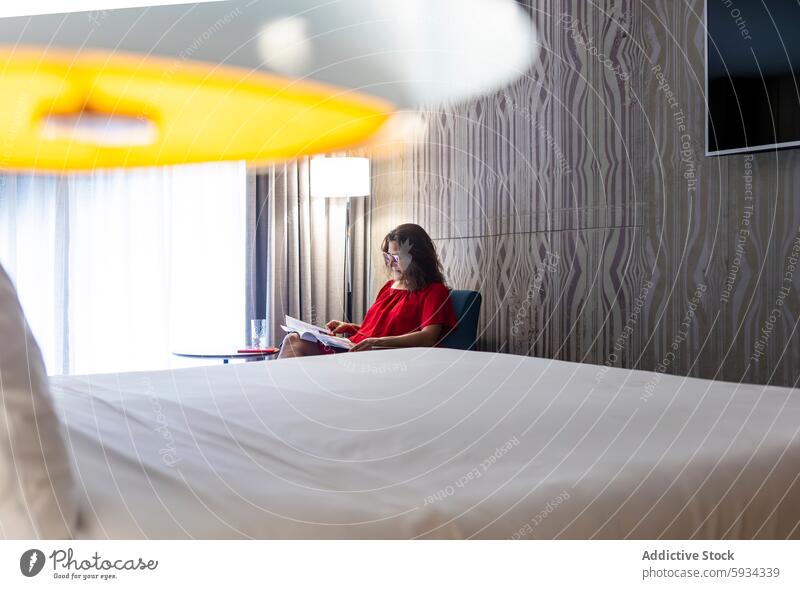 Woman in red dress reading in a stylish hotel room woman modern decor contemporary furniture leisure sitting paper document focus comfort indoor relaxation