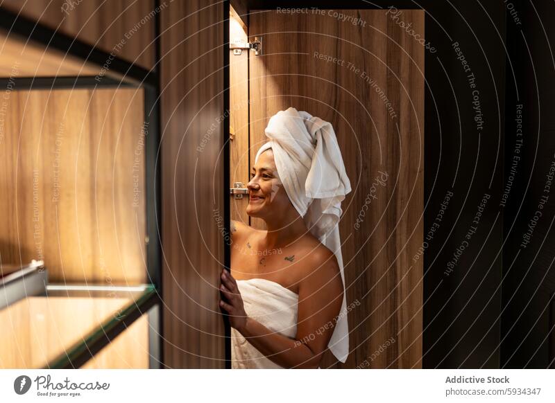 Woman smiling with a towel on her head woman bathroom smile door wood joyful peek modern middle-aged wrapped home interior comfort casual happiness care hygiene