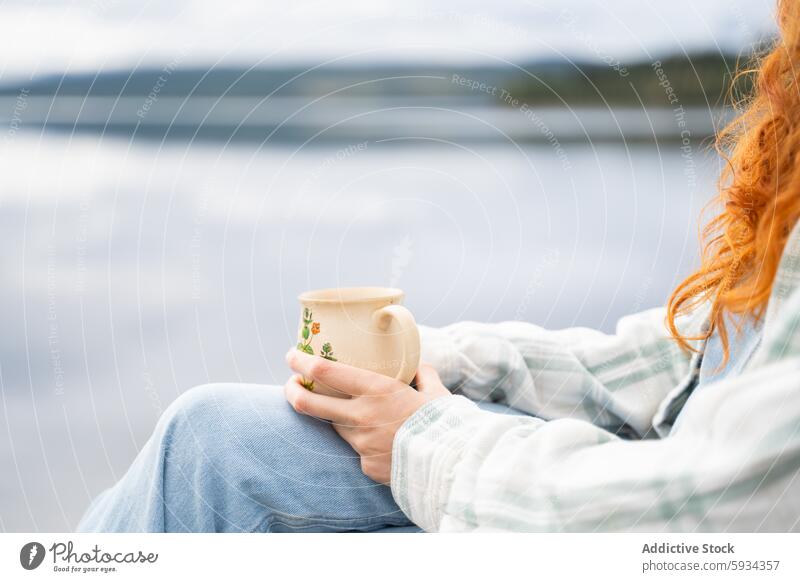 Person holding a mug by a serene lake during camping morning tranquility peace relaxation redhead denim plaid clothing ceramic nature outdoor leisure scenic