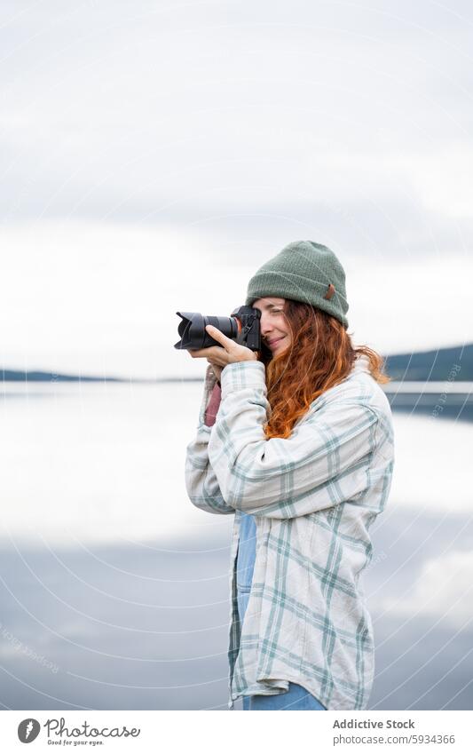 Redheaded woman capturing nature with camera by the lake redhead photography beanie plaid shirt outdoor scenic peaceful water hobby leisure activity environment