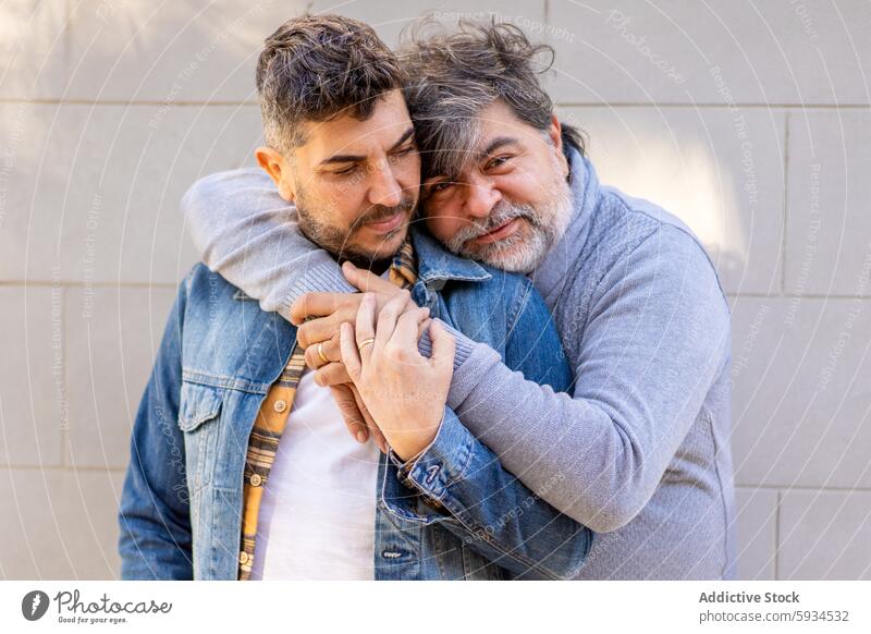 Gay couple embracing in a tender moment together gay man affection embrace tenderness relationship love warmth holding hands adult mature young denim jacket