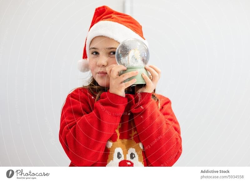 Young girl in Santa hat admiring a snow globe santa hat christmas festive red sweater reindeer holiday season celebration child youth female adorable winter