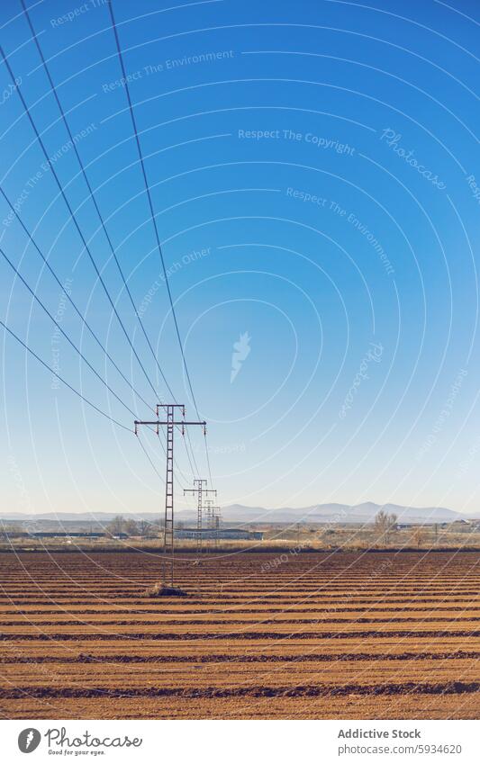 Electric pylons stretching across rural landscape electric power line field plowed sky clear blue tranquil scene electricity infrastructure energy supply