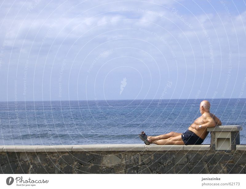 quiet seat Man Wall (barrier) Stone Ocean Swimming trunks Sandal Shuffle Vacation & Travel Bald or shaved head Beer belly Vantage point Tourist Lake Horizon