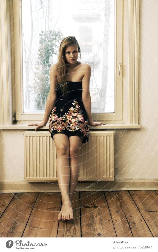 Young woman with long brunette hair and long legs sits on bed in