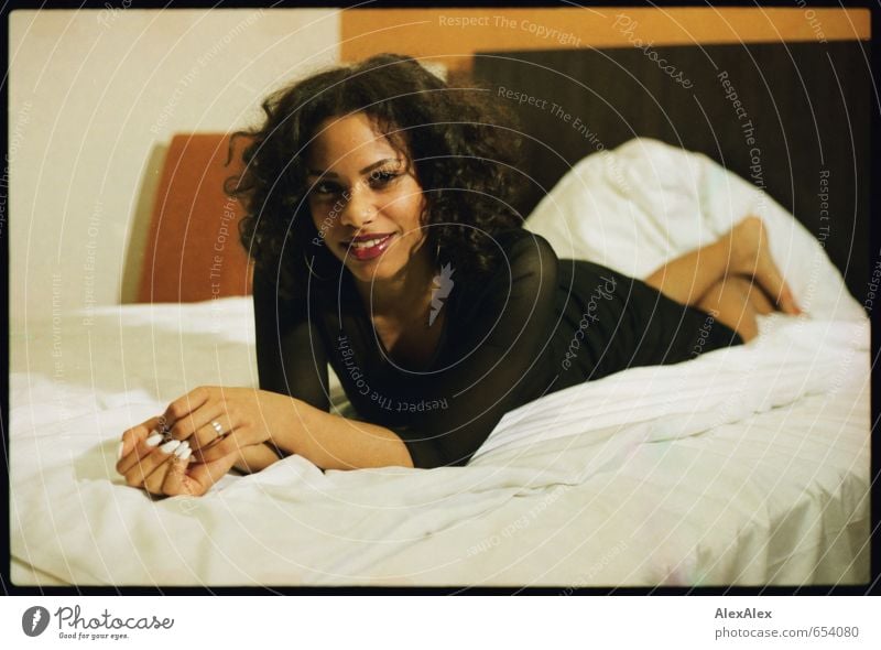 young beautiful dark skinned woman lies on hotel bed and smiles Bed Hotel room Young woman Youth (Young adults) Body Face Hand 18 - 30 years Adults Dress