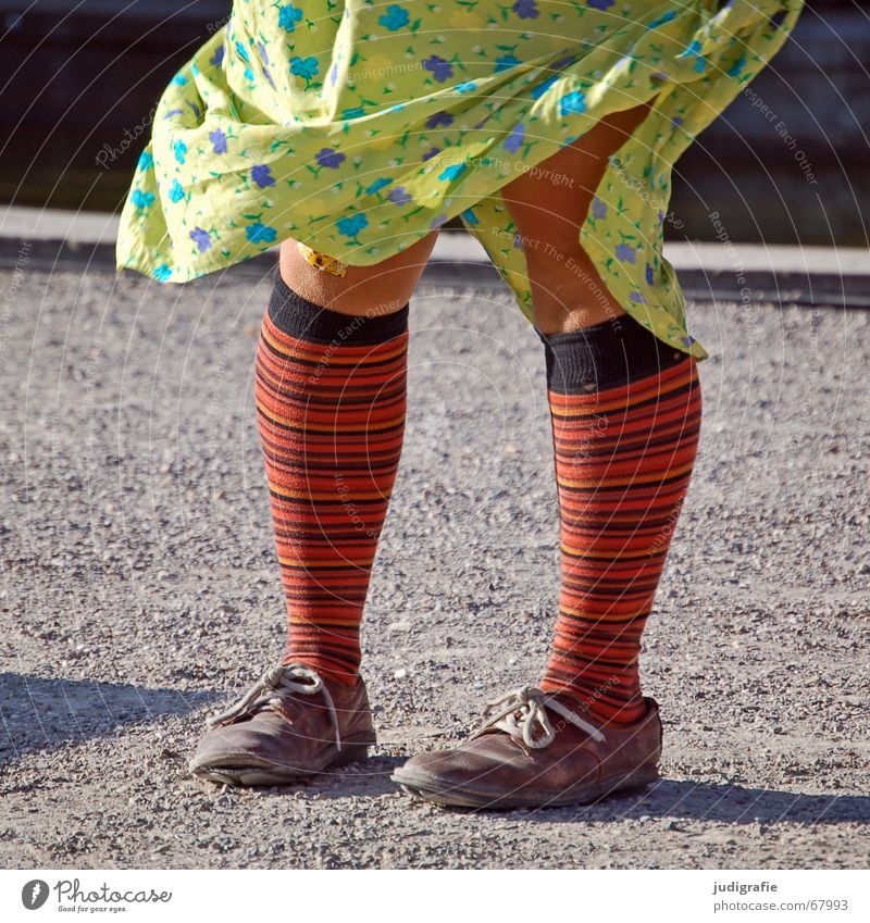 A girl with colorful striped stockings stands on the shadow of a