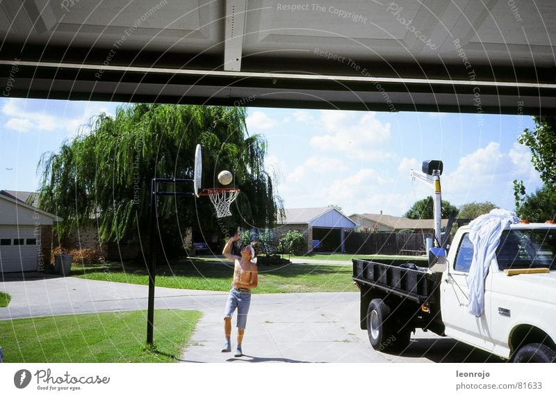 Boy with bare upper body and headband plays basketball in front of the garage. Next to him is a pickup truck Pick-up truck Basketball Basketball basket Americas