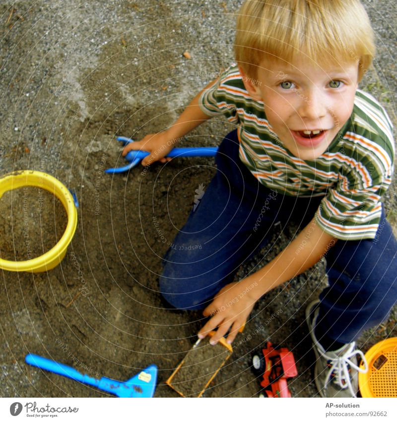 play sand Boy (child) Child Blonde Facial expression Emotions Hand Fingers T-shirt Striped Eyebrow Lips Freckles Think Small Innocent Tub Shovel Truck Tractor